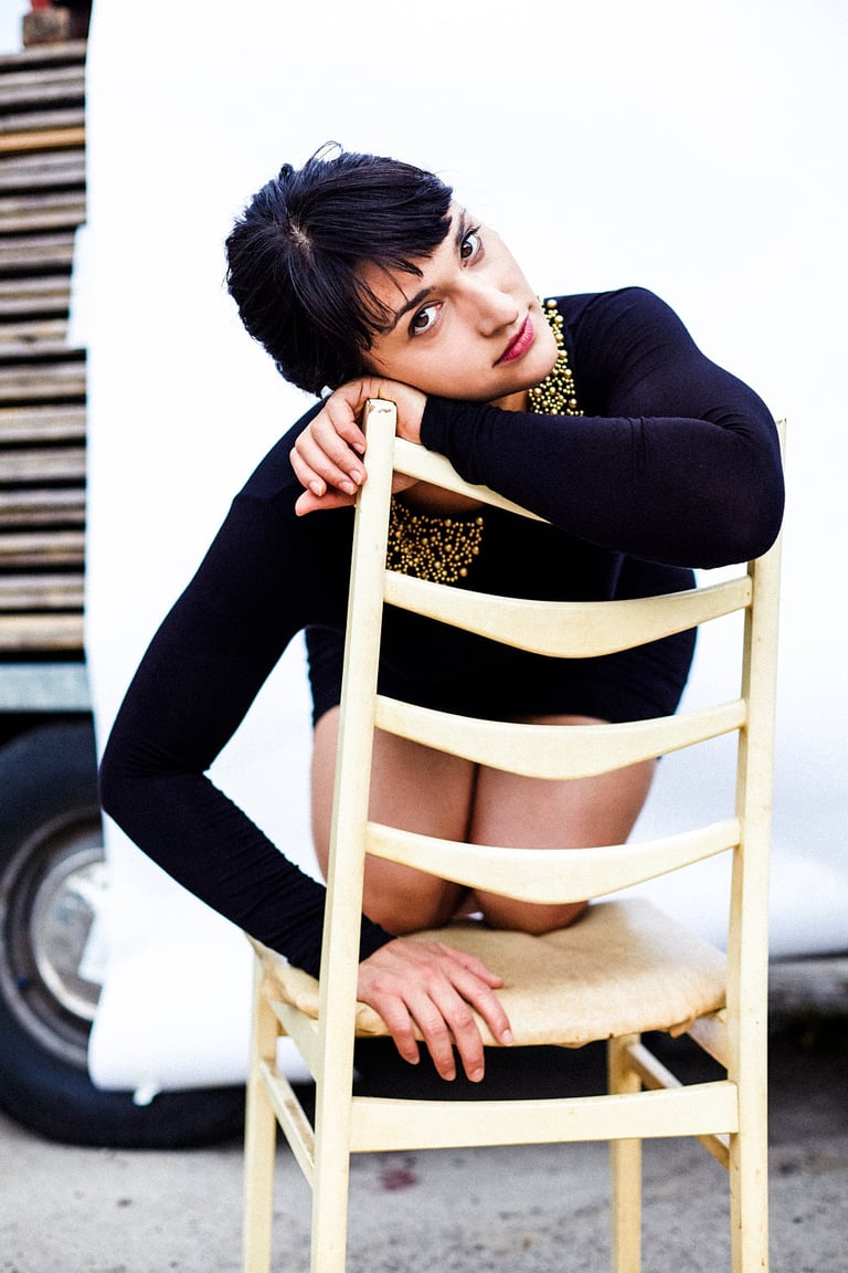 A young woman crouching on a chair in a black dress.