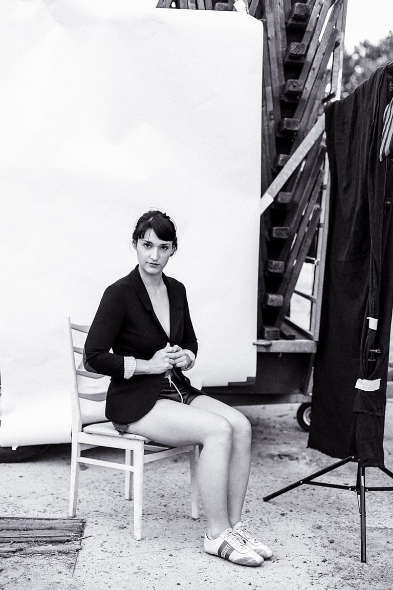 Actress Silvana Veit sitting outdoors in a black jacket and sneakers.