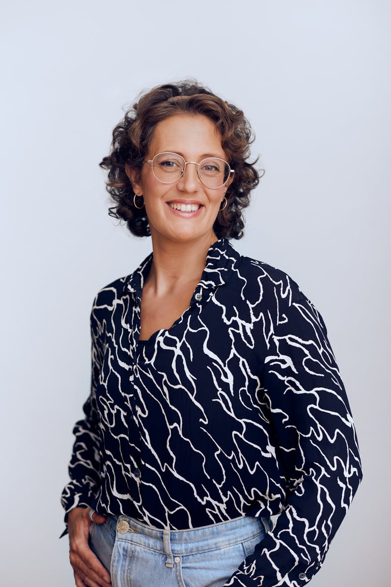 A smiling woman with a patterned shirt photographed in a studio.