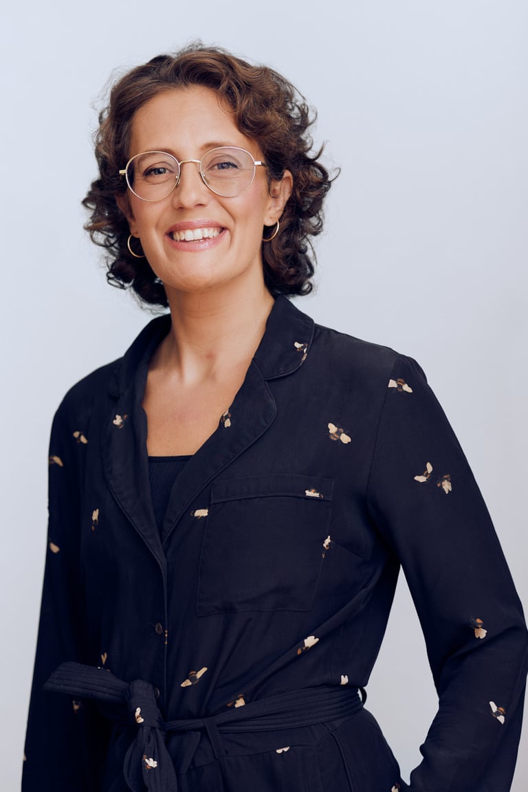 Woman in a dark blue jumpsuit wearing glasses.