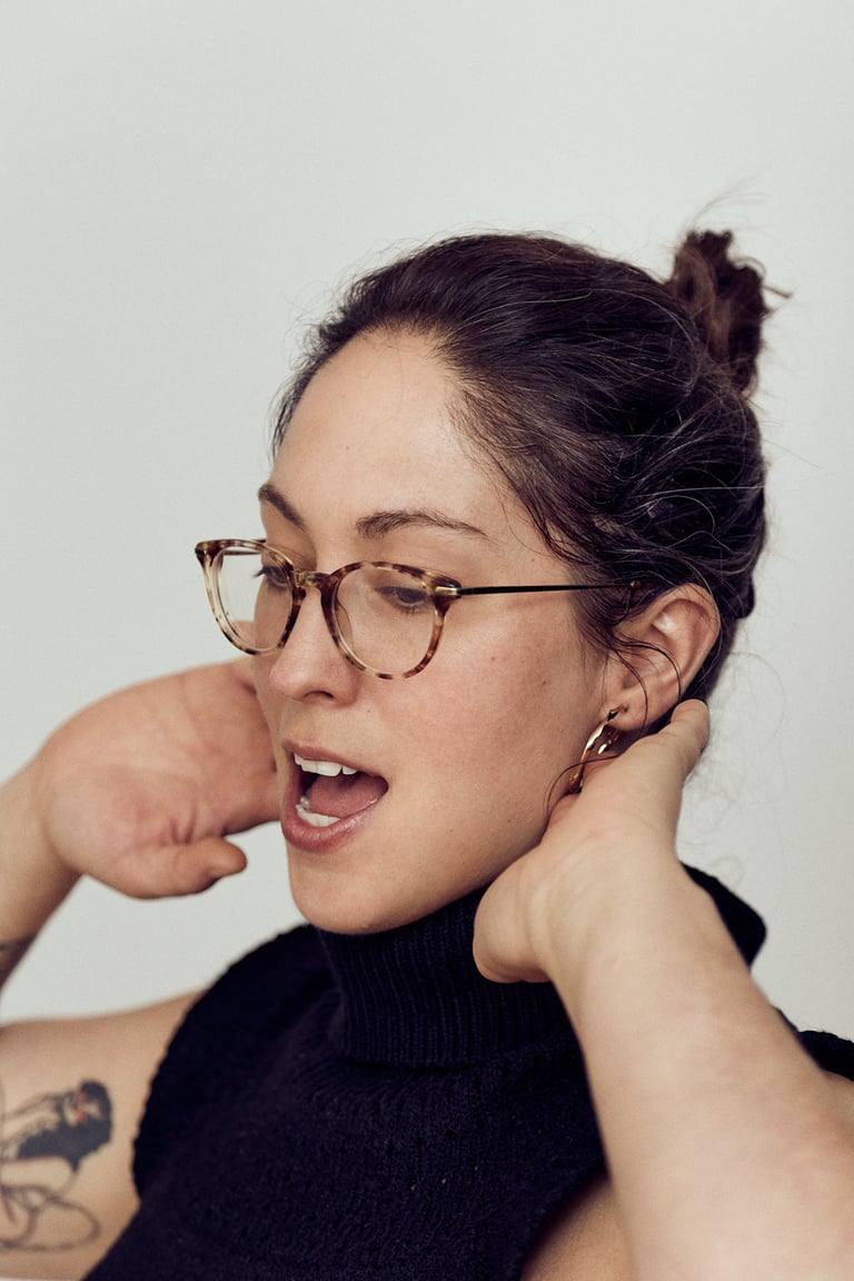 A headshot of a woman wearing glasses singing.