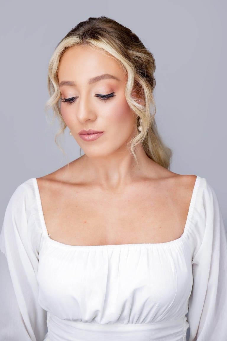 Bride with blonde hair styled softly back, soft glam wedding makeup, glowing skin, long lashes, and natural pink lipstick.