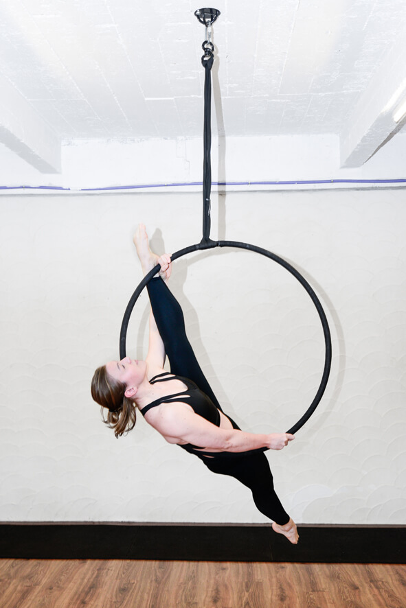 Vrouw in zwarte outfit voert een aerial hoop oefening uit bij De Polecats Fabriek in Gent