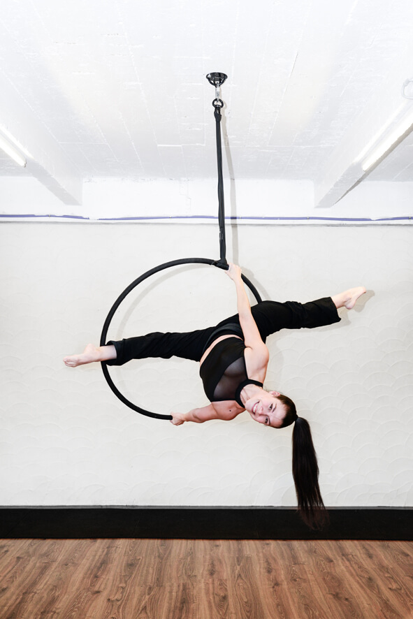 Vrouw in zwarte outfit voert een aerial hoop oefening uit bij De Polecats Fabriek in Gent