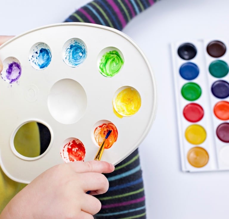 A child holding an art palette mixing colours 