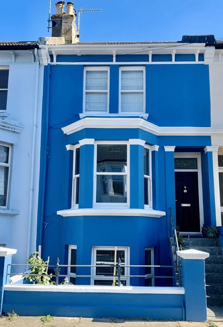 A vibrant blue terraced house with white trim and a large bay window in a residential Brighton area.