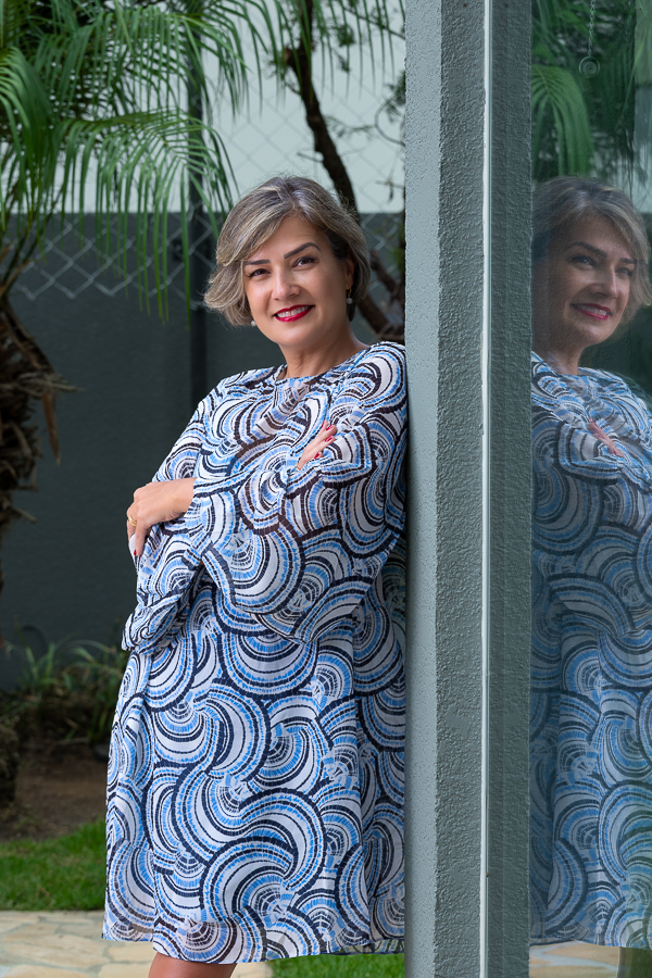 Mulher com vestido estampado, sorrindo, encostada em pilastra, no jardim