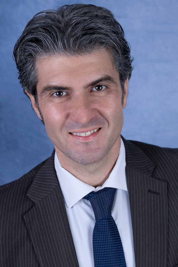 advogado vestindo terno escuro e gravata sorrindo para retrato com fundo azul