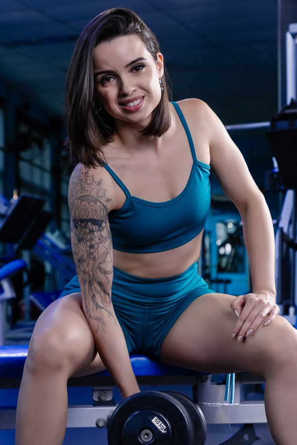 mulher vestindo conjunto fitness azul segurando halteres e sorrindo