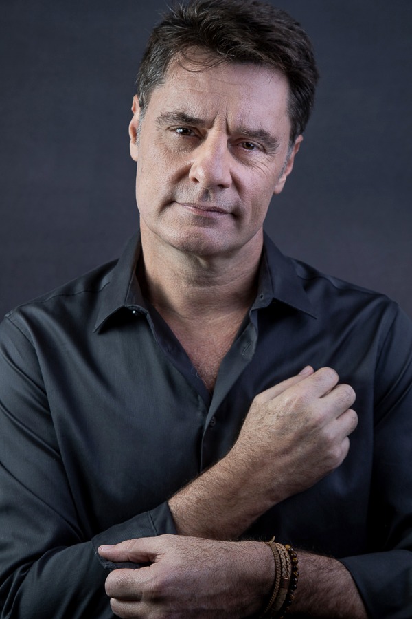 homem vestindo camisa cinza em estúdio com fundo cinza, cruzando os braços