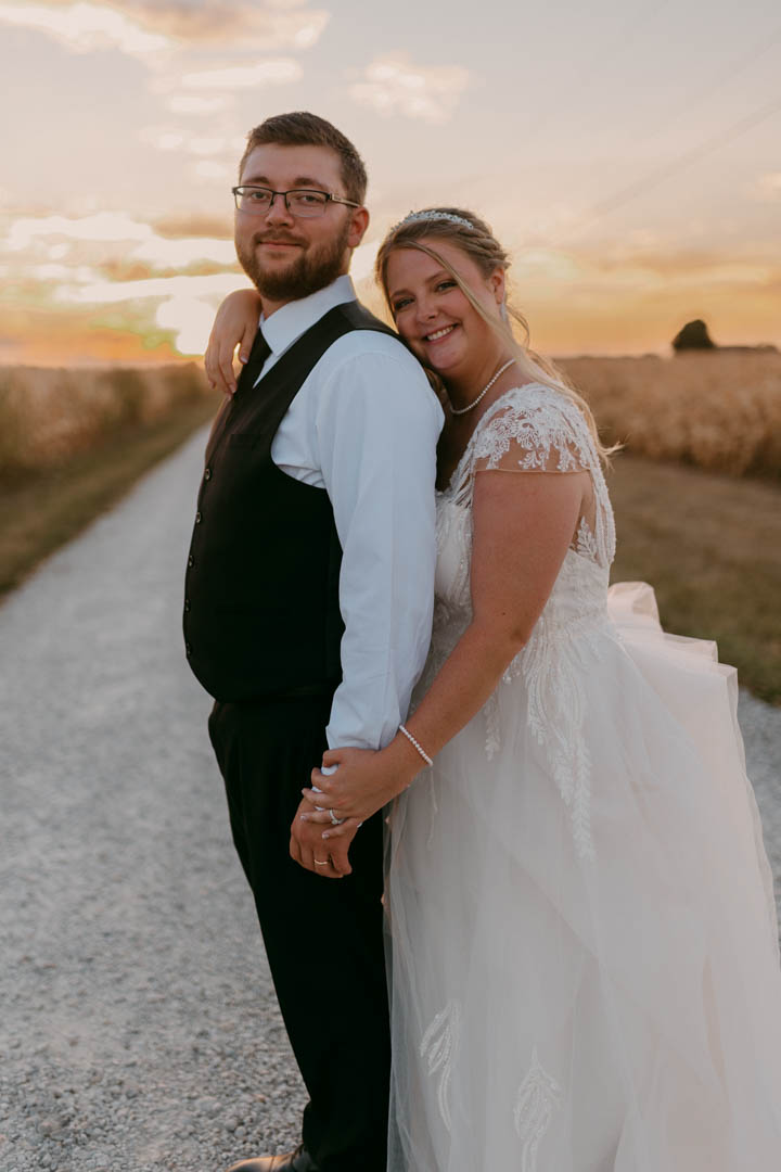 a bride and groom standing in front of a sunset