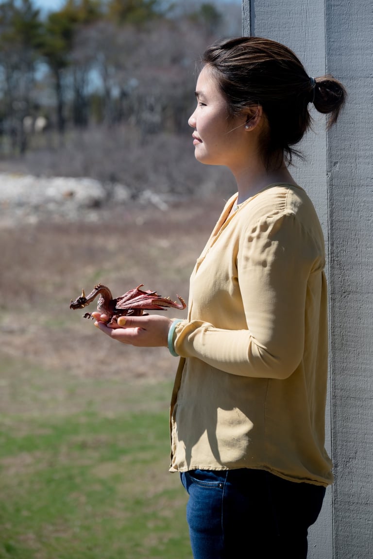 Side profile of a woman holding a small red toy dragon figurine outdoors on a sunny day.