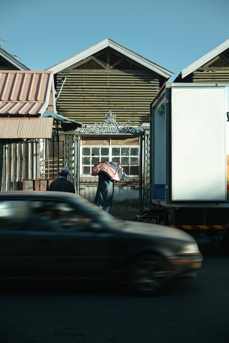 Worker carrying sack at rear entrance of Port Louis market, with passing cars