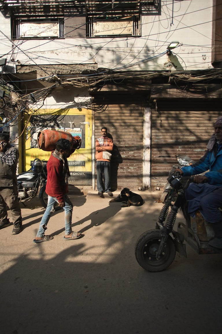 Pedestrians and a motorbike passing closed shops on an Old Delhi street.