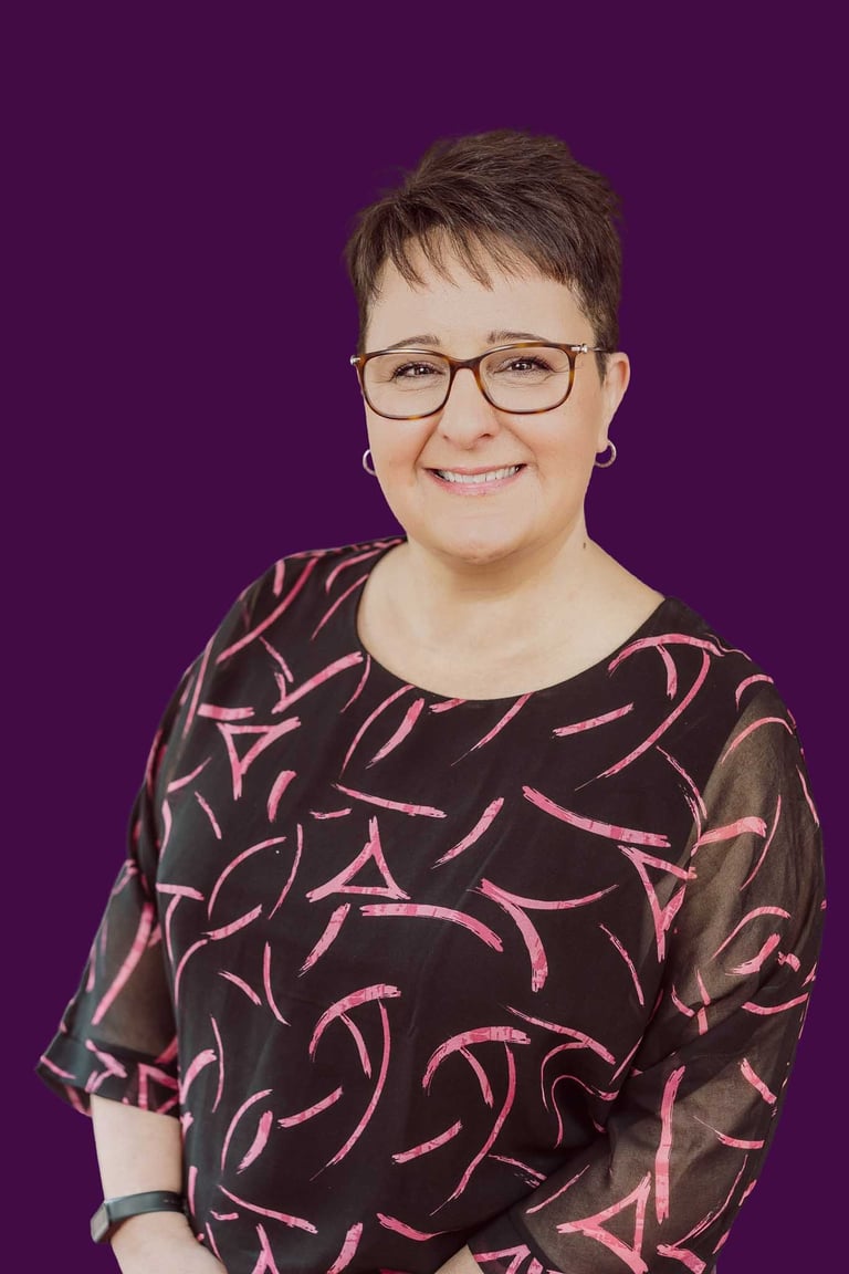 Professional portrait of a smiling woman with glasses and short hair on a purple background.