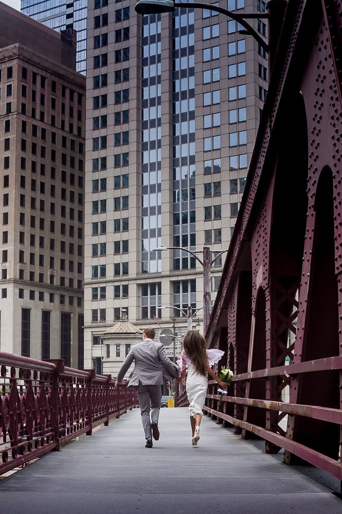 pareja de novios corriendo por puente de ciudad 