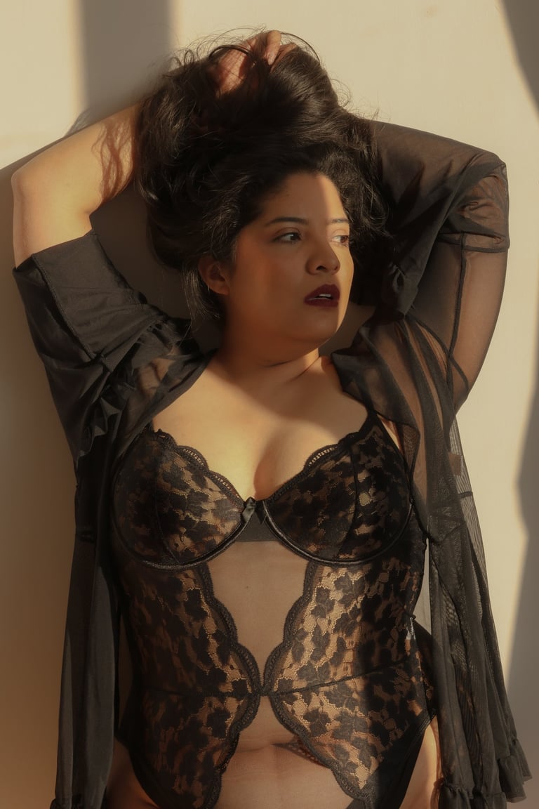 Una mujer de talla grande vistiendo un body de encaje negro y una bata transparente con luz natural 