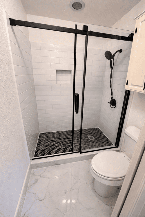 Modern bathroom renovation featuring a walk-in shower with black frame glass doors and white subway tile.
