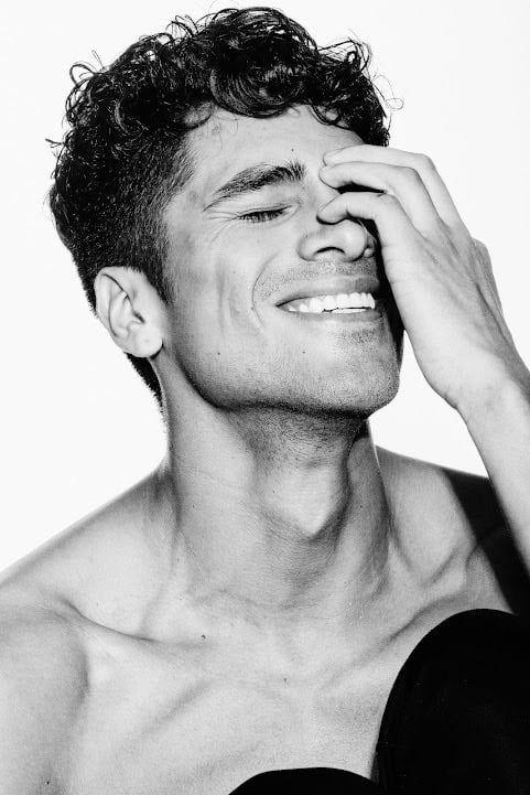Black and white portrait of a smiling Dany Peña with curly hair and hand on his face.