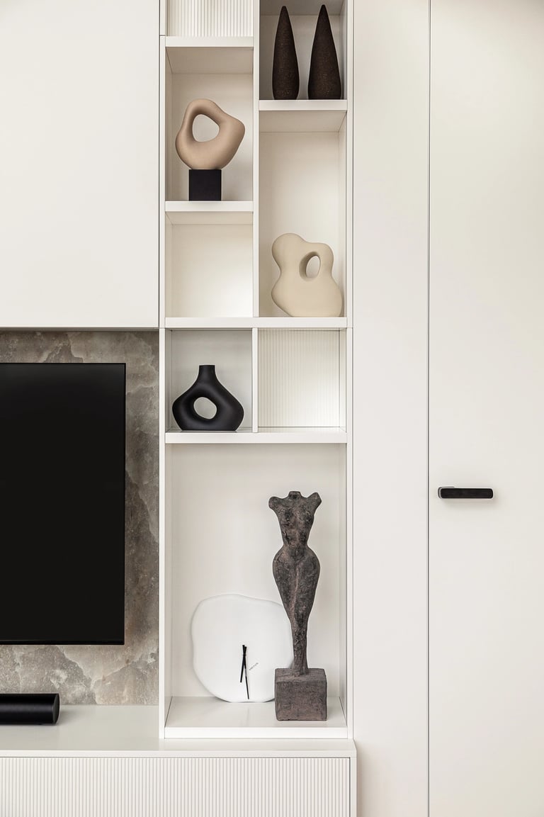 Biały regał z nowoczesnymi rzeźbami w minimalistycznym salonie.