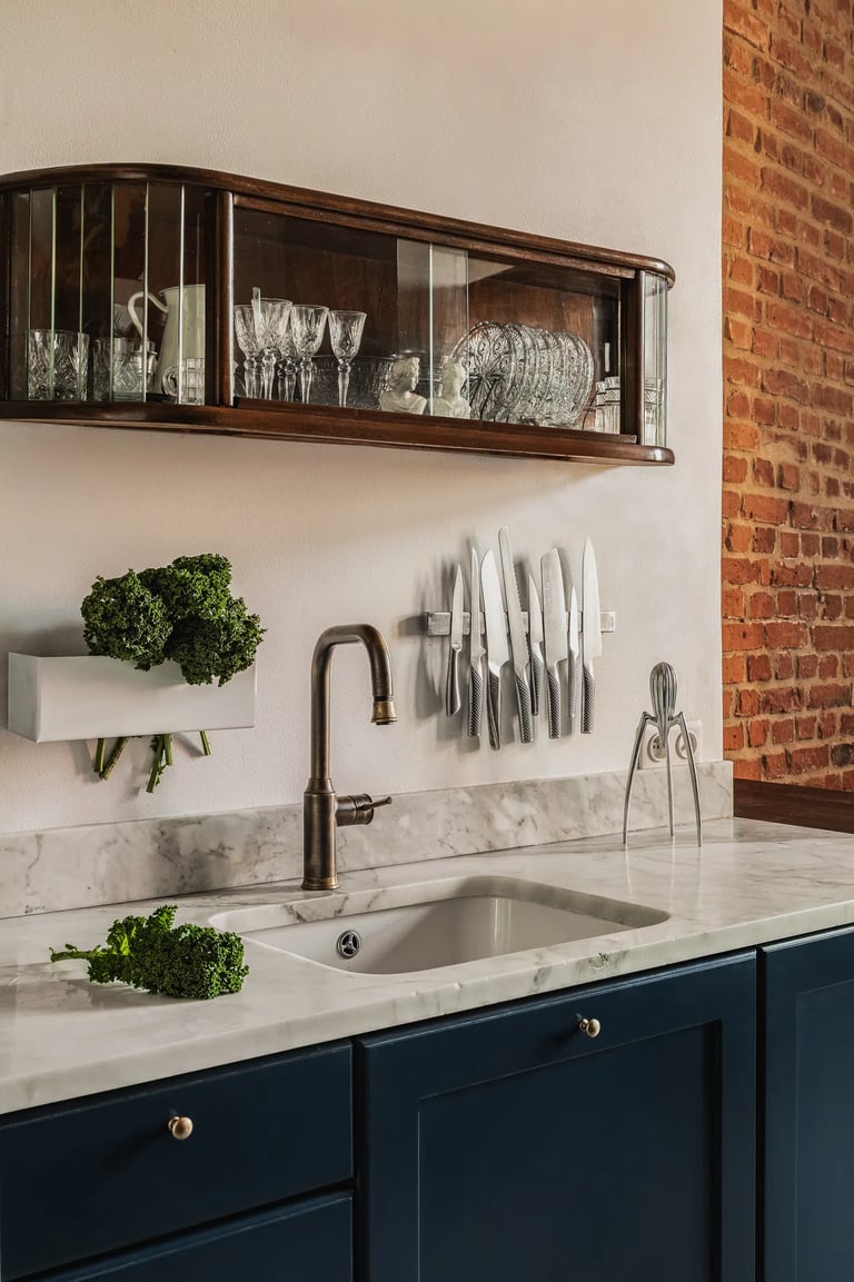 Granatowa kuchnia, marmurowy blat i wisząca witryna vintage.