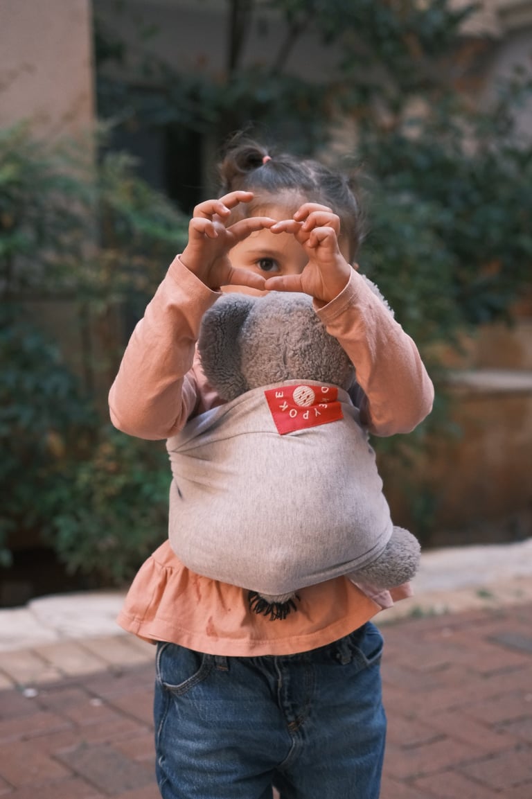 a little girl holding a stuffed animal in a babywrap carrier