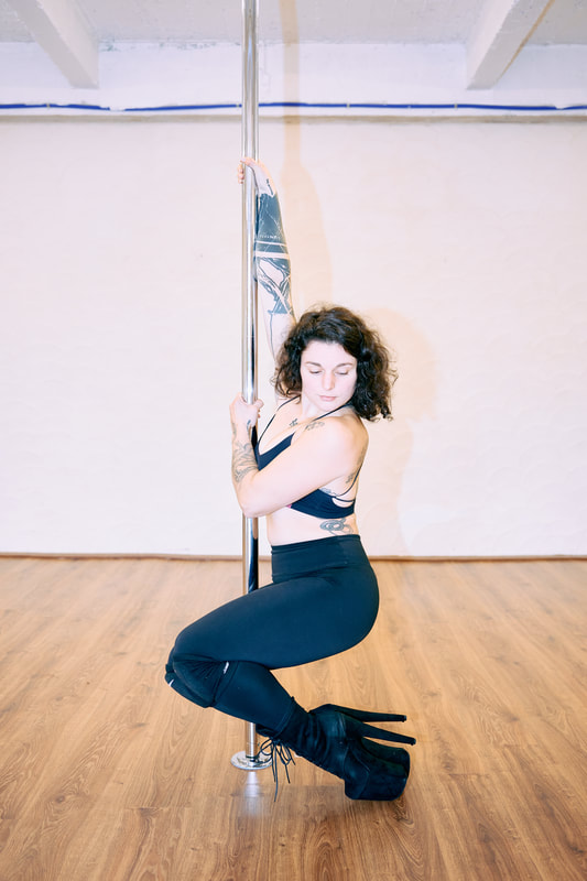 Vrouw in zwarte top poseert met paaldanspaal bij De Polecats Fabriek in Gent