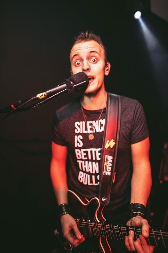 Guitarist Lucas Vianna playing a Red Special Brian May guitar while singing into the microphone.
