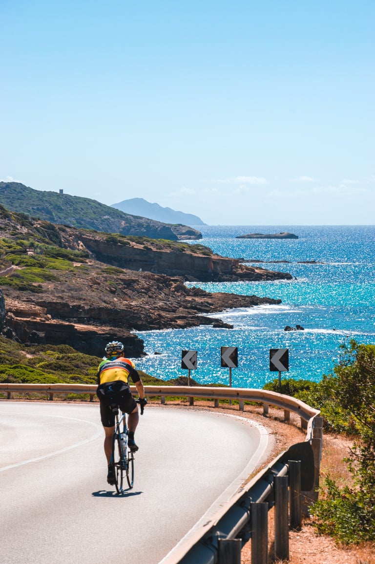 Cyclist on the scenic Alghero-Bosa road in Sardinia with Mediterranean sea view.