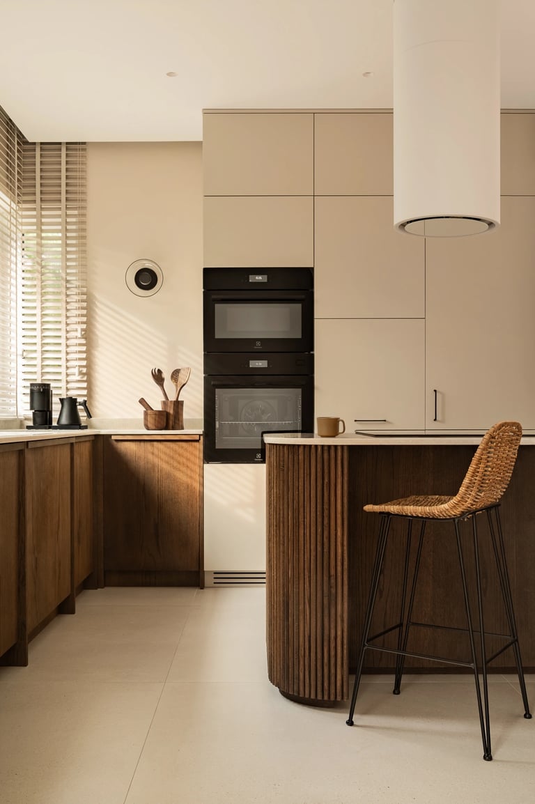 Fotografia kuchni: beżowa zabudowa, zaokrąglona wyspa i gra światła.