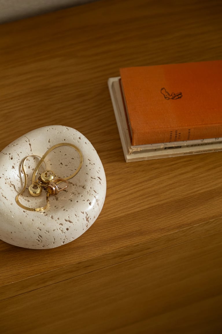 Kamienna misa z trawertynu ze złotą biżuterią na drewnianej szafce.