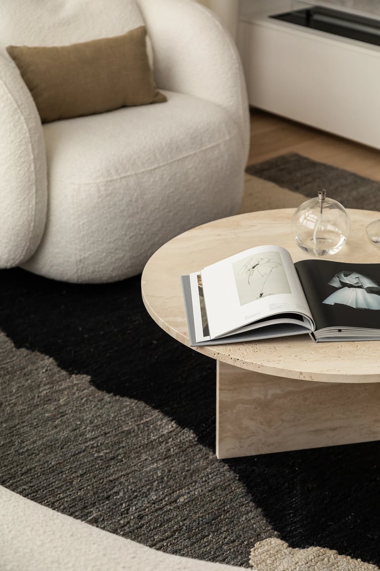 Okrągły trawertynowy stolik kawowy z albumem – detal wnętrza.