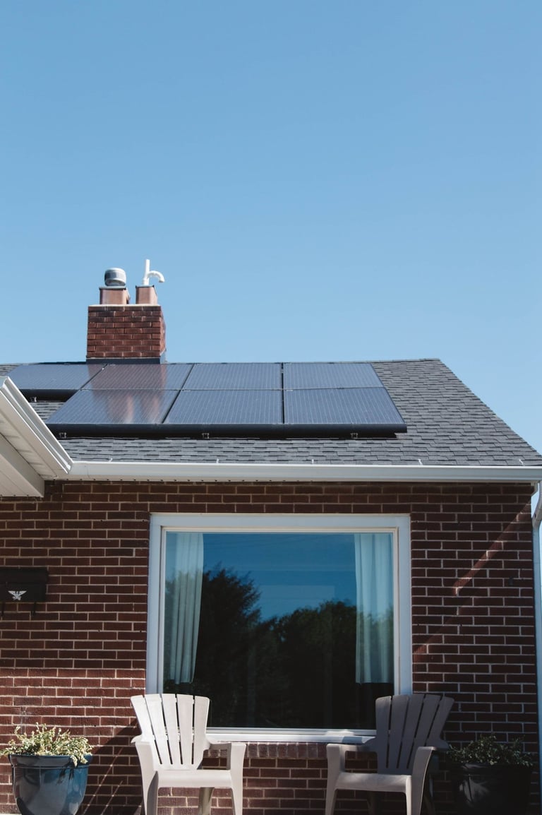 Modern solar panels installed on a residential dark shingle roof of a brick house.