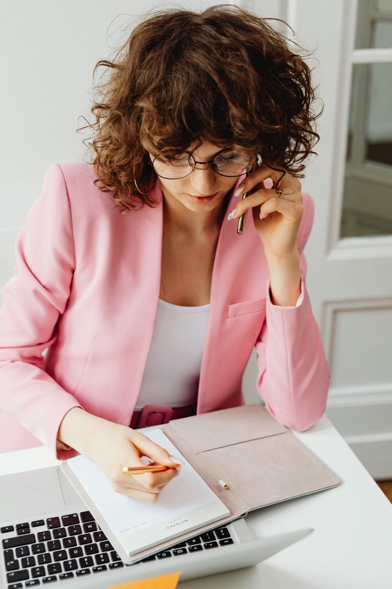 A laptop and open notebook on a desk with a female taking notes.