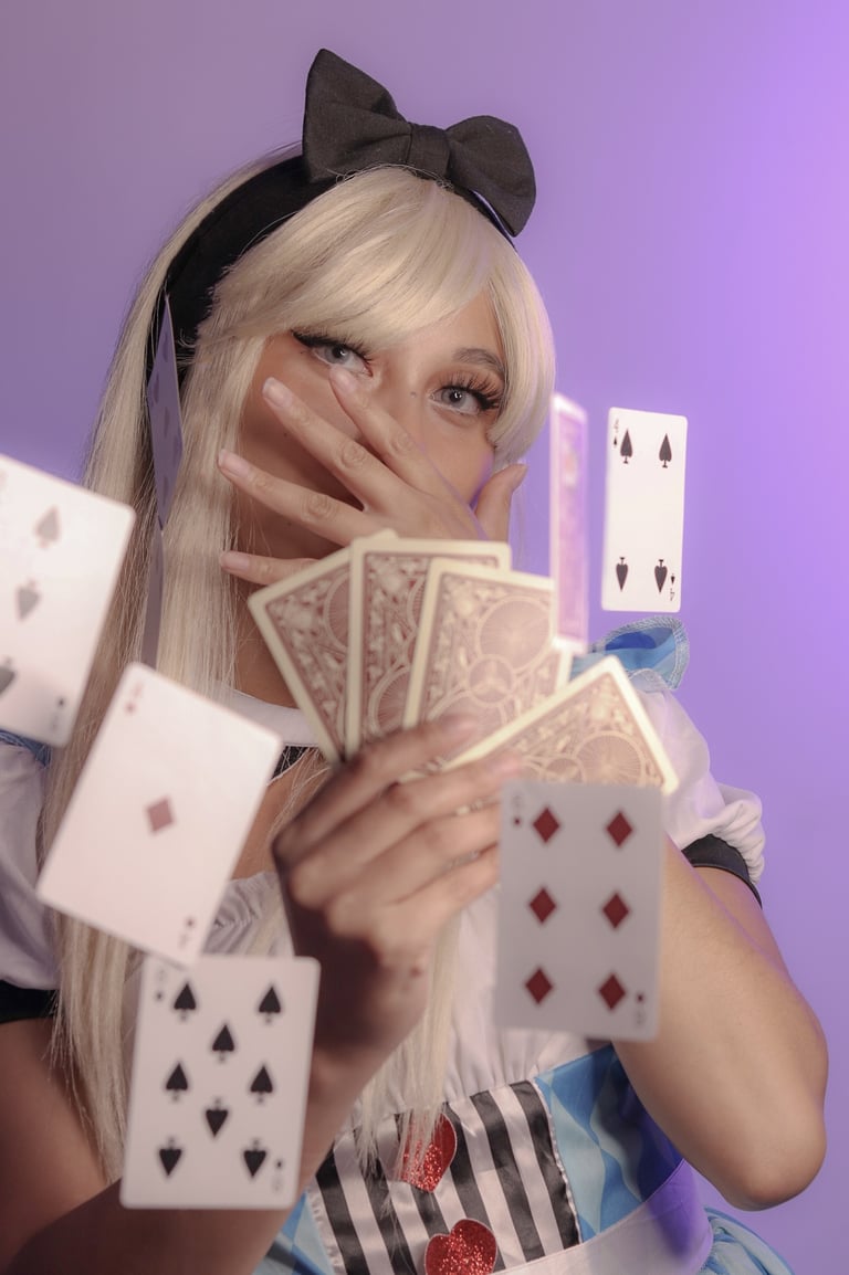 Playful costume of Alice in Wonderland holding playing cards, more cards floating in the air. 