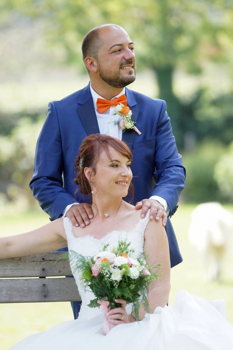 photo de couple pendant un mariage. la mariée est assise avec son bouquet comportant du orange