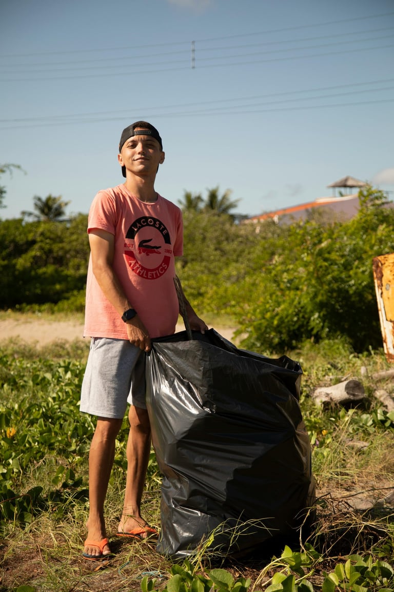 A young volunteer holding a large black trash bag during a community beach cleanup project.