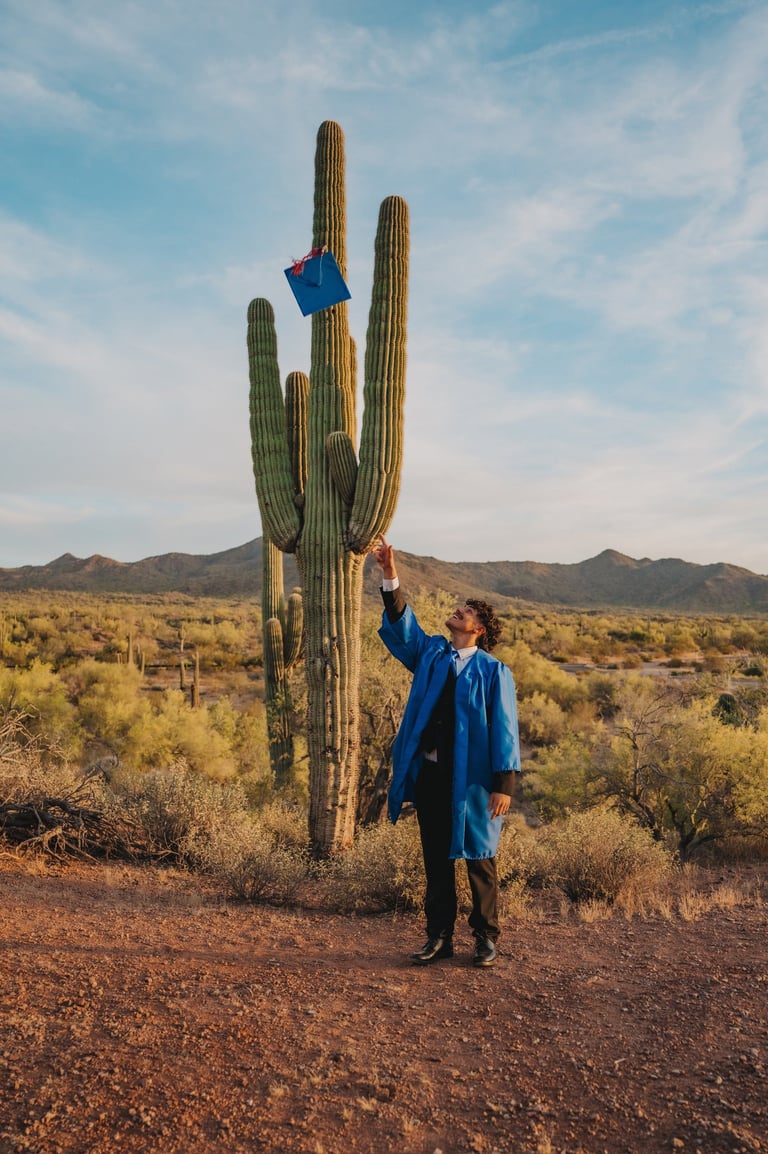 A college graduate in a blue gown tosses his cap onto a tall saguaro cactus in the Arizona desert.