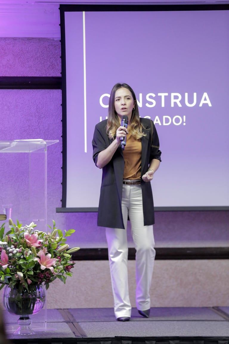 uma mulher em pé encima de um palco, em frente a um projetor de imagens com um microfone