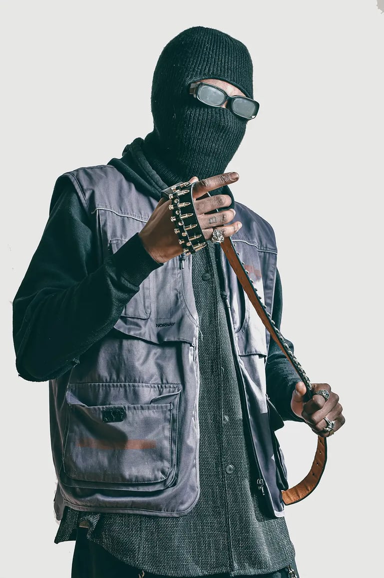 Studio photo of a man in a black jacket and a mask on, holding a belt