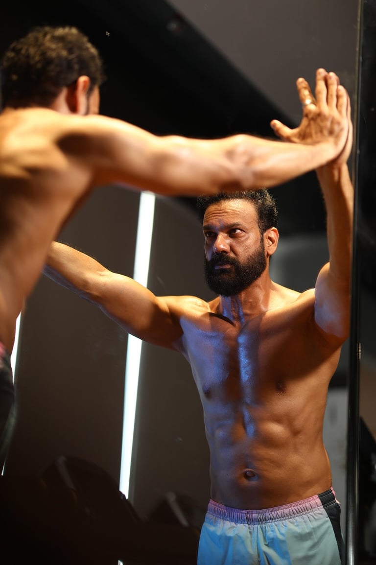 Shirtless man looking in mirror and evaluating himself and thinking about his fitness
