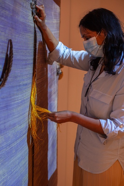 Masked woman with long black hair uses a tactile screen made of invasive grass and natural objects.