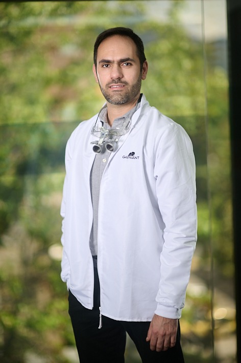 Professional male dentist in a medical coat wearing dental loupes and standing in a clinic