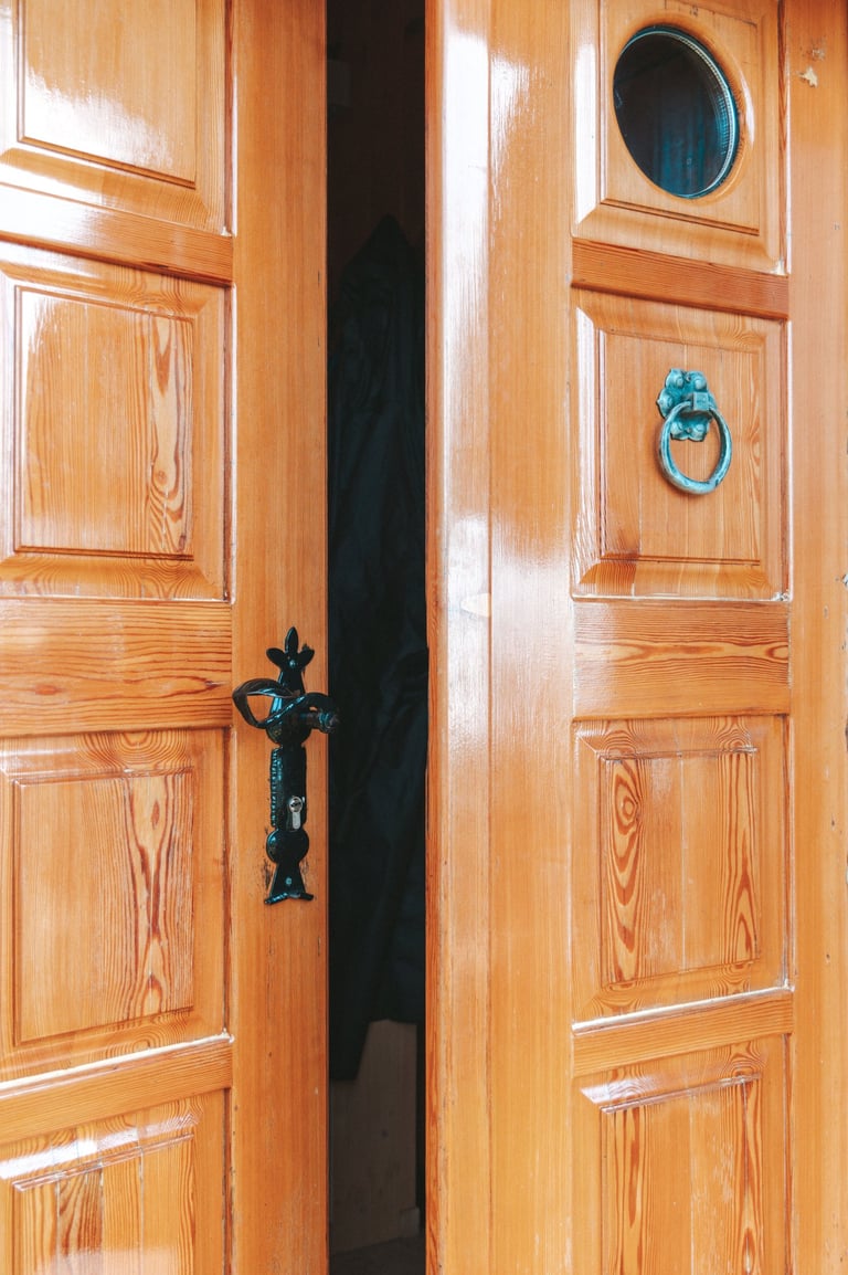 Polished wooden double doors slightly ajar with vintage metal hardware and a small circular window.