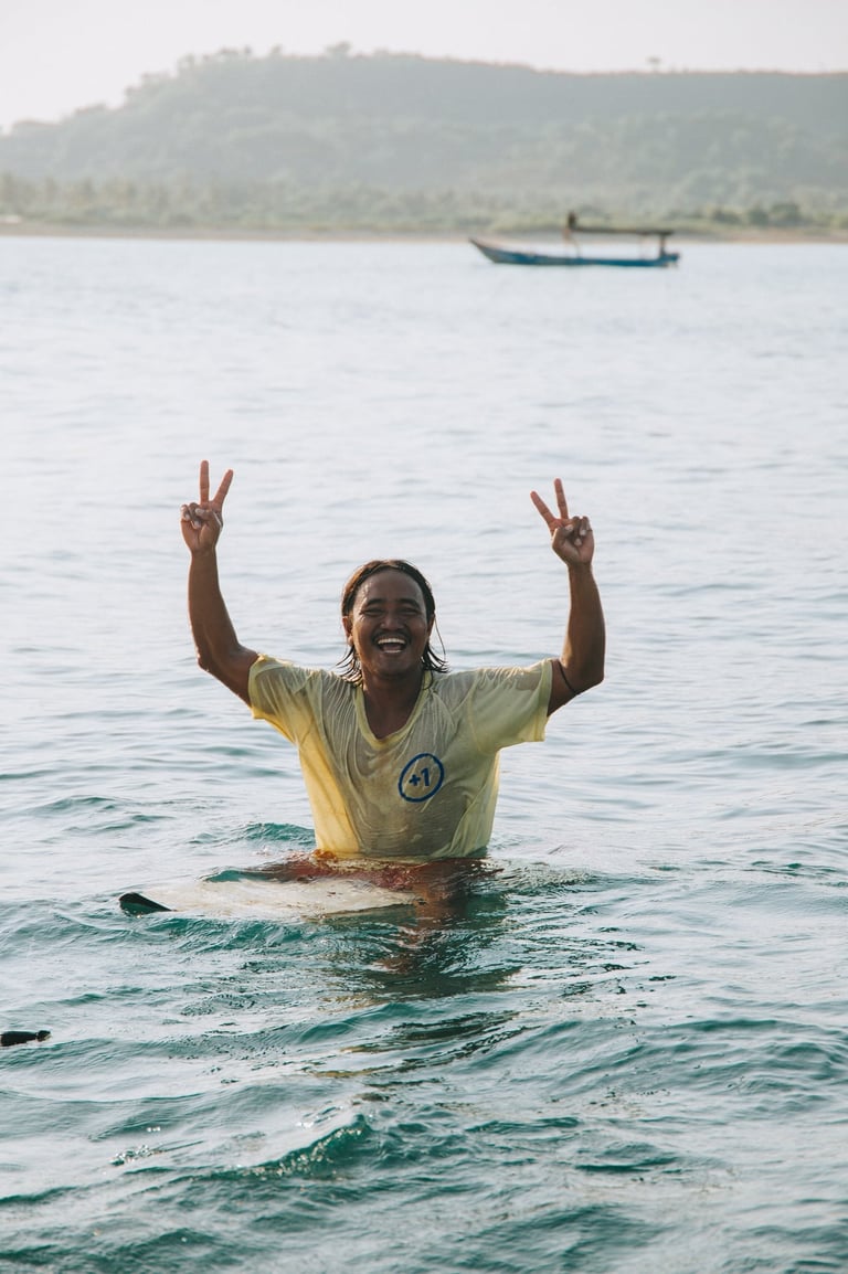 Smiling local surfer in tropical water making peace signs while sitting on a surfboard.
