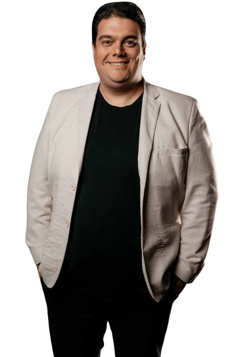 Danïel Sbeghem portrait of a smiling man in a beige blazer and black shirt against a dark background