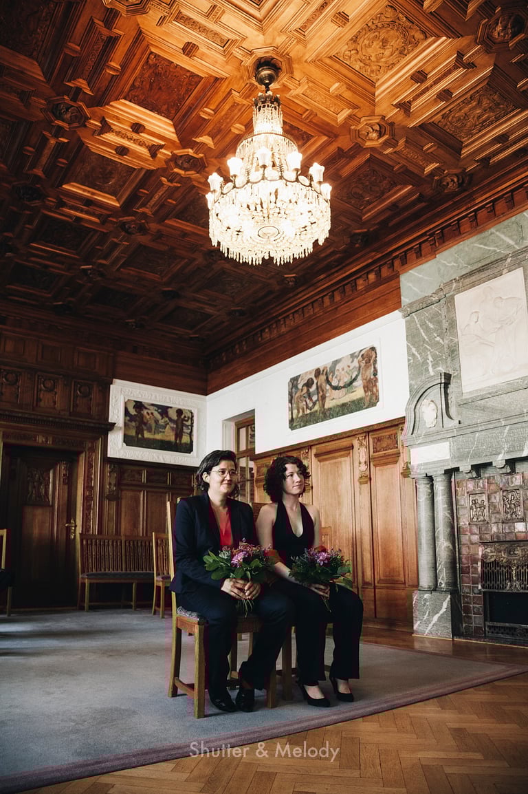 Brides sitting in the Pankow town hall under a chandelier.