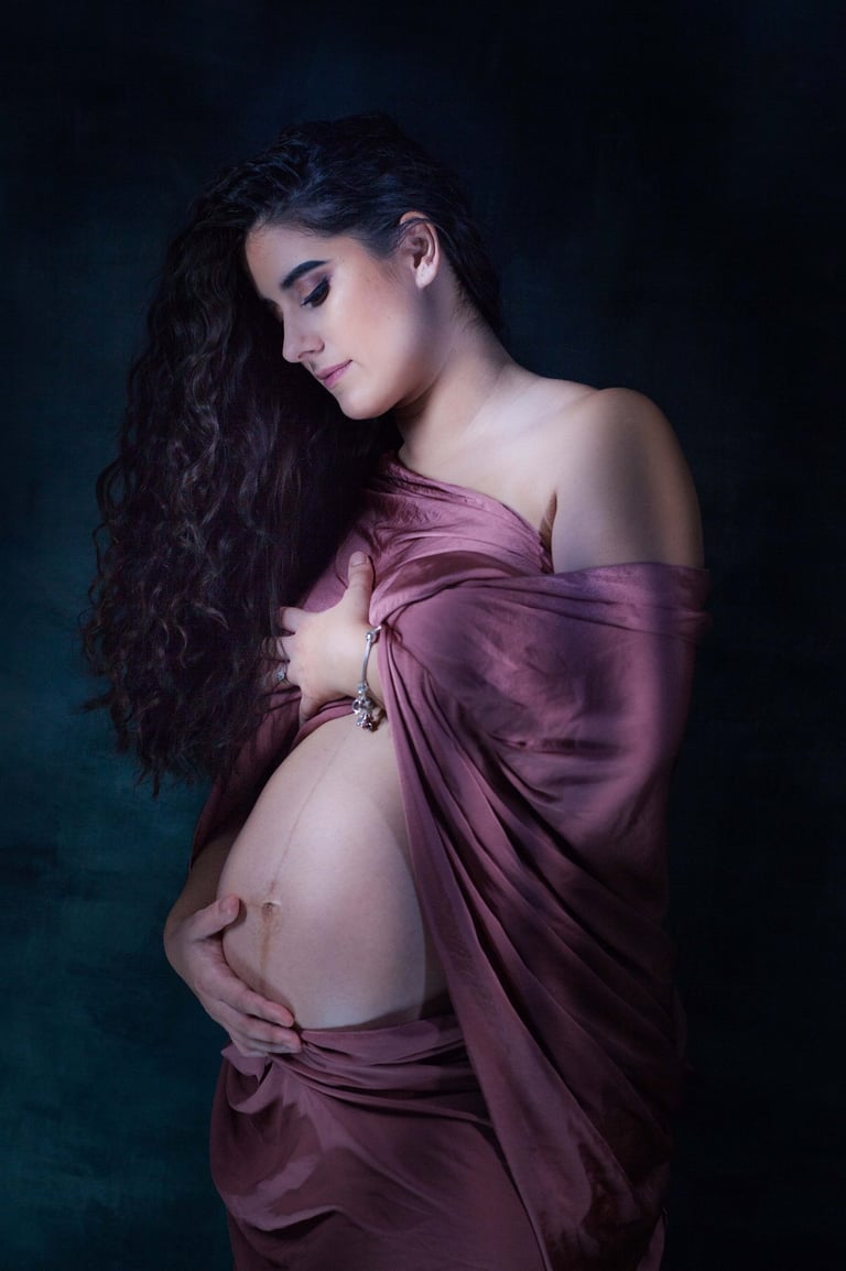 Femme enceinte drapé d'un voile pourpre antique caressant son ventre rond et baissant son regard