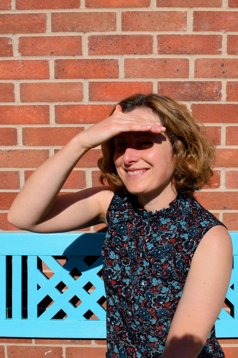 I am looking out past the camera to the garden, smiling, and shading my eyes from the sun