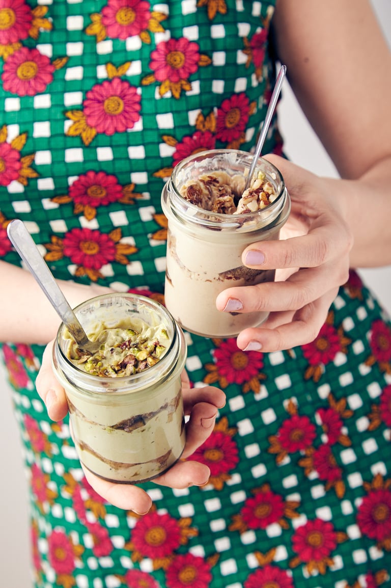 Woman in a flower dress holding two jars of tiramisu.